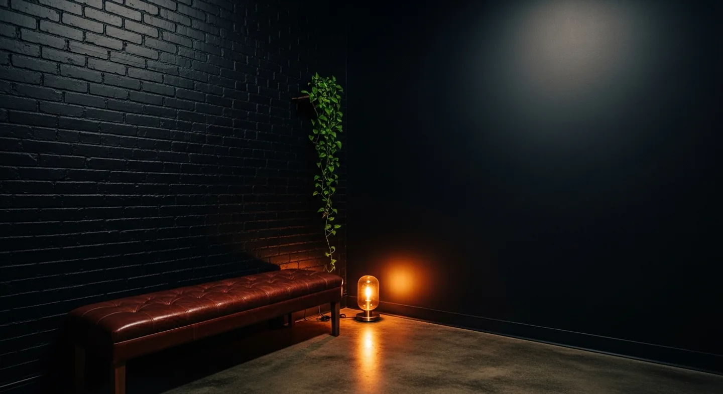 The studio's small waiting area: black painted brick, a worn leather bench, a trailing plant and a low lamp on a concrete floor